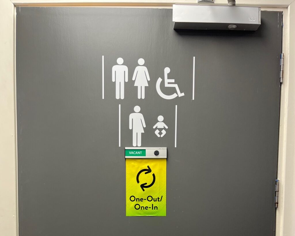 Door of toilet showing male, female, disabled, nonbinary, baby icons.