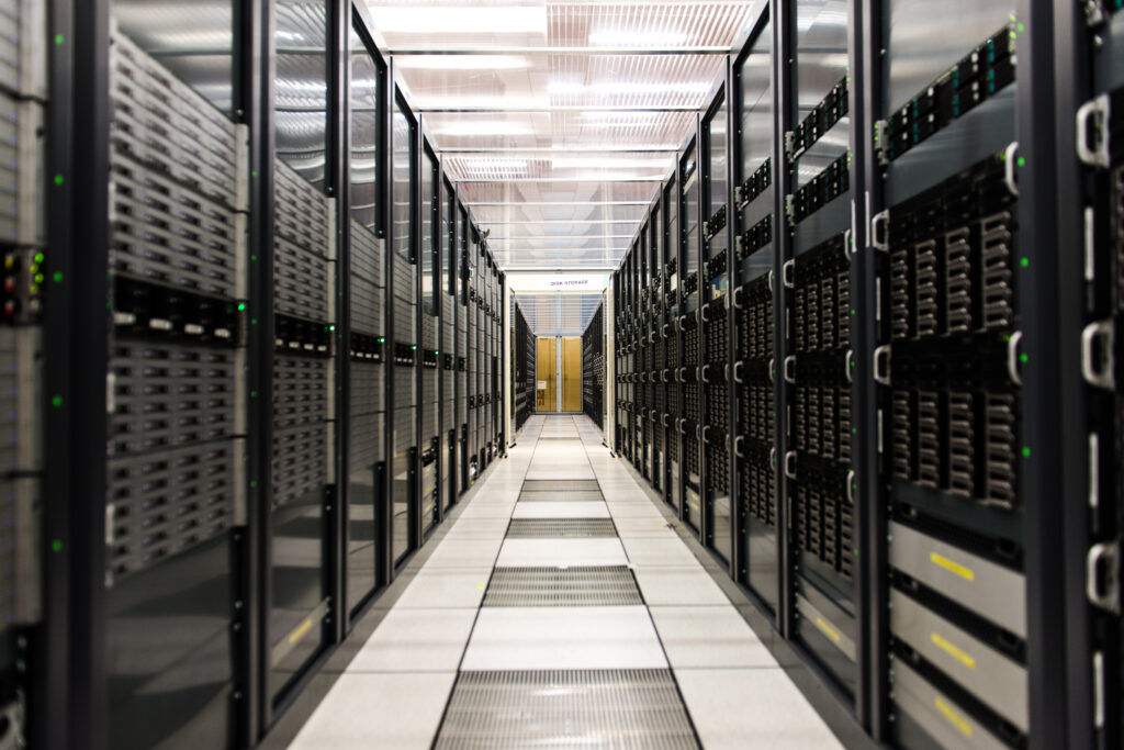 A long corridor of computer mainframes with grey doors. Bright white floors and lights above.